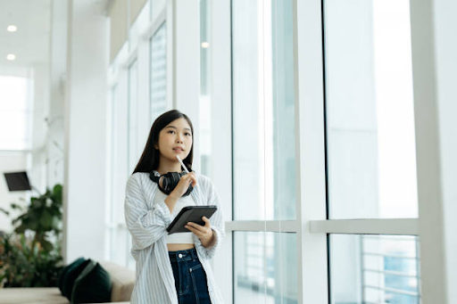 A woman holding a tablet and thinking while looking out the window, related to applying for a Dubai residence visa.